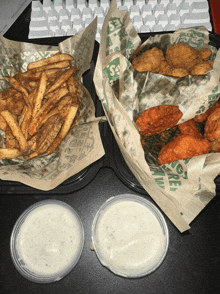 two containers of chicken wings and french fries with dipping sauces on a table