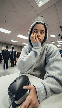 a girl wearing a hoodie is sitting at a table with a computer mouse