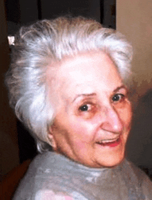 an elderly woman with gray hair and a grey turtleneck smiles for the camera