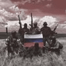 a group of soldiers are posing for a picture with a russian flag in a field .