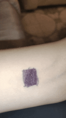 a close up of a person 's arm with a small square of purple paint on it