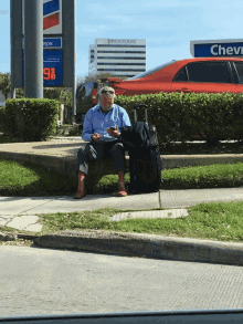 a man sits on the curb in front of a gas station that says 98