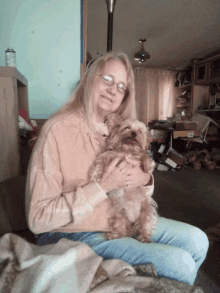 a woman with glasses is holding a small brown dog