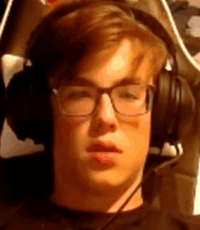 a young man wearing glasses and headphones is looking at the camera .