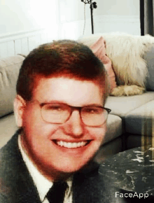 a man wearing glasses and a tie is smiling in front of a couch .