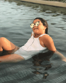 a young girl wearing sunglasses and a white tank top is floating in a pool