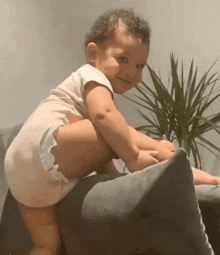 a baby in a diaper is sitting on a pillow and smiling .