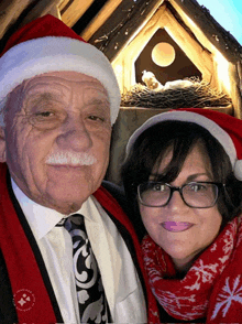 a man and a woman wearing santa hats pose for a picture in front of a nativity scene