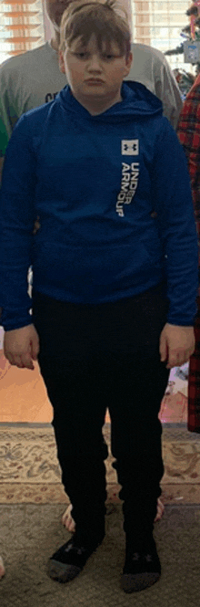 a young boy wearing a blue under armour hoodie and black pants