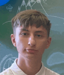 a young man is standing in front of a chalkboard in a classroom .