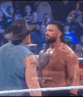 a man in a cowboy hat stands next to a shirtless wrestler in a wrestling ring .