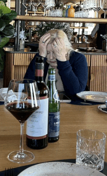 a woman is sitting at a table with a bottle of wine and a glass of wine