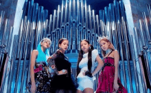 a group of four women are standing next to each other in front of a large pipe organ .