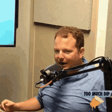 a man in a blue shirt is sitting in front of a microphone with a sign that says too much dip