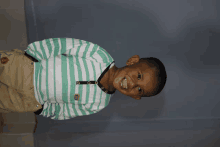 a young boy in a green and white striped shirt smiles for the camera