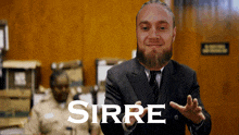 a man in a suit and tie says sirre in front of a brown wall