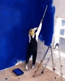 a person is standing on a ladder and painting a wall blue