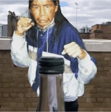 a man with long hair is standing in front of a brick wall and a bottle