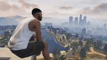 a man in a white tank top is sitting on a ledge overlooking a city