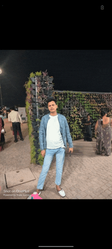 a man is standing in front of a wall of plants on a sidewalk