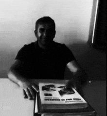 a man is sitting at a table holding a book that says ' a ' on the front