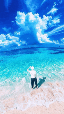 a man in a white hat stands on a beach looking at the ocean