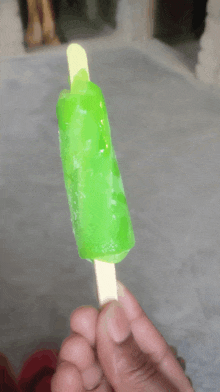 a person is holding a green ice cream bar on a stick