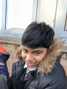 a young boy wearing a black jacket with a fur hood smiles