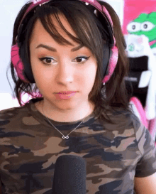 a woman wearing headphones and a camo shirt is looking at the camera .