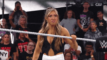 a woman stands in a wrestling ring with a crowd behind her and a sign that says ny on it