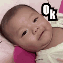 a baby is laying on a pink pillow with the word ok on it