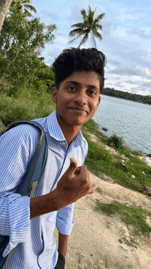 a young man in a blue striped shirt is giving the thumbs up sign