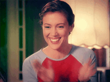 a woman wearing a red and blue shirt is smiling and clapping her hands .