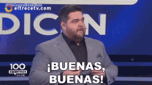 a man in a suit stands in front of a screen that says " buenas "