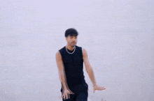 a man wearing a black tank top and black pants is dancing in front of a white wall