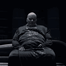 a bald man is sitting in a dark room wearing a black robe