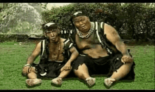 two men are sitting next to each other on the grass in a park .