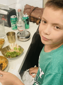 a boy sits at a table with a can of sprite and a bottle of vitaly water