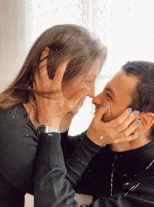 a man and a woman are touching their noses and the woman has blue nail polish on her nails