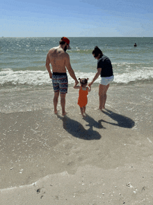 a man with a tattoo on his back holds hands with a woman and child on the beach