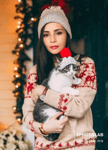 a woman holding a cat with a santa hat on her head