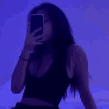 a woman is taking a selfie with her phone in front of a purple background .