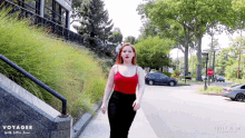 a woman in a red tank top is walking down a sidewalk in front of a sign that says stop