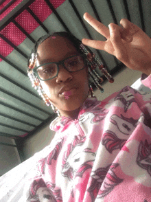 a young girl wearing glasses and a pink unicorn blanket giving a peace sign