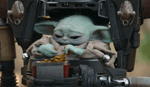 a baby yoda is sitting on a machine eating a snack