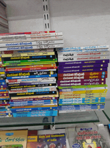 a stack of books including gods and goddesses of india sits on a glass shelf