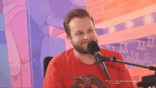 a man in a red shirt is sitting in front of a microphone with a brick wall in the background