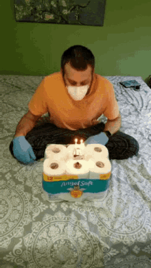 a man wearing a mask and gloves is sitting on a bed with a box of angel soft toilet paper