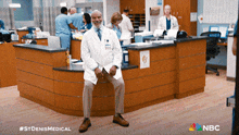 a man in a lab coat sits on a counter in a hospital with the nbc logo in the background