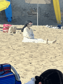 a woman in a bathrobe sits under an umbrella on a beach